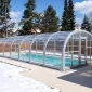 Winter pool enclosure beside a northern residential home with snow around the pool deck